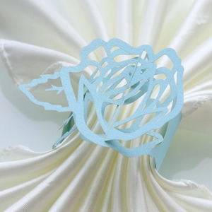 Macro detail of laser-cut light blue rose paper napkin ring on a white satin napkin