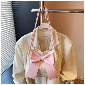 Détail du sac seau en paille tressée avec grand nœud en cuir rose et fines bandoulières