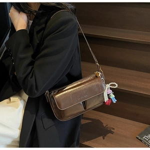 Detail view of brown glossy leather pillow bag with charms and embossed logo
