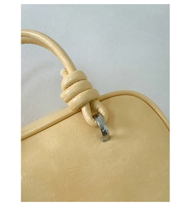 Detailansicht einer hellgelben Handtasche mit Knotengriff und silbernen Metallbeschlägen