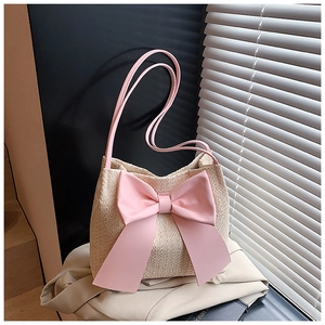 Détail du sac seau en paille tressée avec nœud en similicuir rose et fines bretelles