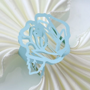 Detailed macro view of a light blue laser-cut rose paper napkin ring on white satin