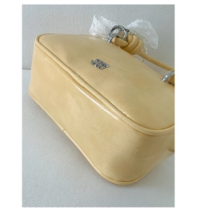 Detail einer cremegelben Handtasche aus Leder mit Falten und einer weißen Spitzenschleife