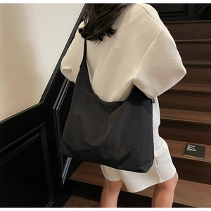Side view of a large black nylon tote bag on a model showing the minimalist crescent shape