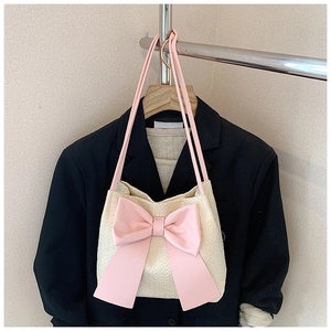 Détail d'un sac seau en paille avec un grand nœud rose, suspendu à un cintre
