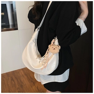 Detail of white half-moon bag featuring crocodile pattern leather and plush bear charm