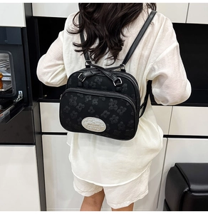 Détail d'un sac à dos noir avec texture florale et plaque de logo argentée chic