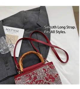 Detailed view of red embroidery bag featuring bamboo handles and red leather strap