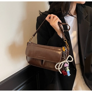 Detail of a brown glossy leather shoulder bag with pearl bow and cartoon doll charms