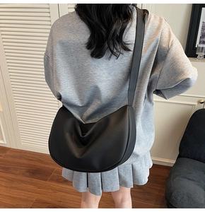 Detail of black pebbled leather crescent hobo bag with wide shoulder strap worn by model