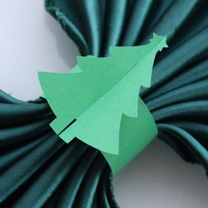 Détail d'un rond de serviette en papier vert sapin sur une serviette en satin vert foncé