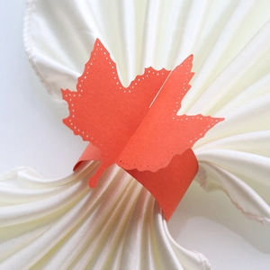 Macro detail of red maple leaf paper napkin ring with laser-cut hollow dots on silk