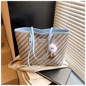 Détail du sac cabas tissé à rayures bleues et jaunes avec anses en cuir et pompon