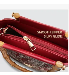 Detail of red bucket bag showing smooth gold zipper and bamboo style handle
