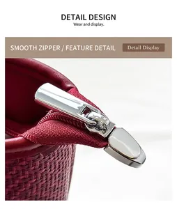 Detail view of the silver metal zipper and red leather trim on a woven tote bag