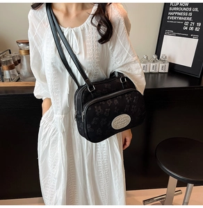 Détail du sac bandoulière noir avec texture florale porté par un mannequin dans un café
