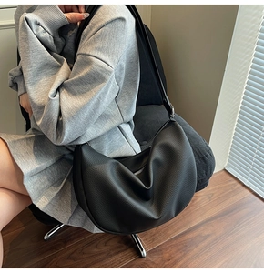 Detailed view of a black lychee texture leather hobo bag with metal zipper on a chair