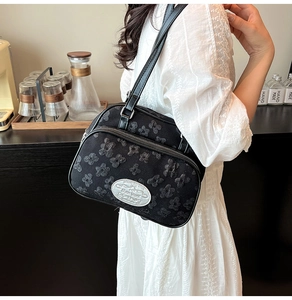 Détail du sac à bandoulière noir avec broderie florale et logo métallique argenté