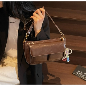 Detail of dark brown oil wax leather pillow bag with vintage gold hooks and brand logo
