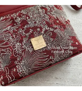 Close-up of red jacquard embroidery fabric with gold logo plaque on a retro crossbody bag