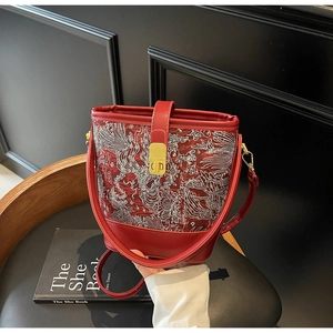 Macro detail of red bucket bag featuring white traditional Chinese bird embroidery and gold clasp