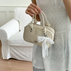 Nahaufnahme einer cremefarbenen Handtasche mit Knotengriff und zarter Spitzenschleife