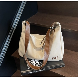 Detail der beigen Canvas-Tasche mit braunem Lederriemen und TCT-Stickerei auf Holztreppen