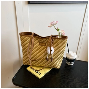 Détail du sac cabas tissé avec bordure en cuir marron et charm sur une table