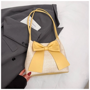 Détail du sac seau en paille avec grand nœud jaune sur une veste grise