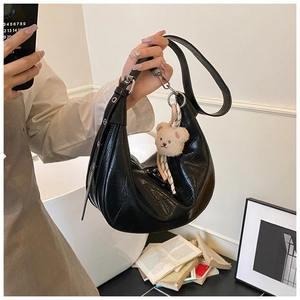 Close-up of black crocodile embossed handbag with a cute plush bear charm accessory