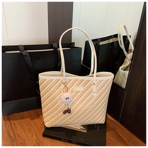 Détail du sac cabas en paille tissée avec motif rayé, plaque de marque et breloque peluche