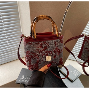 Detail of red embroidered bucket bag featuring bamboo handles and phoenix pattern