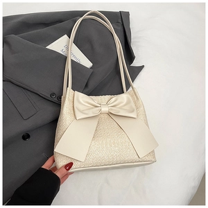 Détail de la texture en paille tressée et du grand nœud en cuir crème sur le sac seau chic