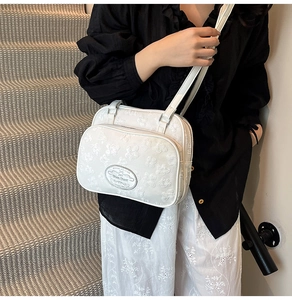 Détail du sac bandoulière blanc avec broderie florale et compartiments à double fermeture