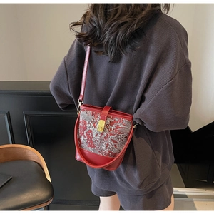 Detail of red bucket bag featuring silver embroidery and golden twist lock on a model
