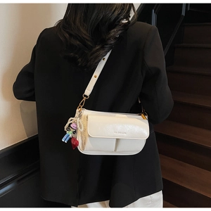 Detail of white crossbody pillow bag with charms worn by a model in a black blazer