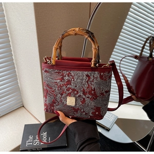 Close-up of dark red bucket bag with bamboo handle and detailed phoenix embroidery