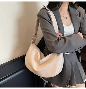 Close-up of off-white lychee texture leather crescent bag worn over a grey blazer