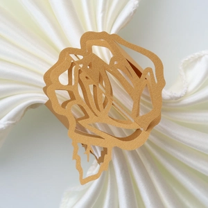 Close-up of laser-cut gold rose paper napkin ring on a white silk table setting