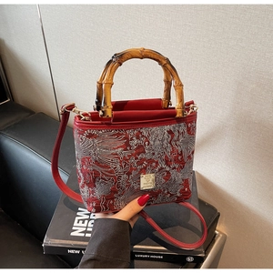 Detailed embroidery on a red bucket bag with bamboo handle and golden hardware accent