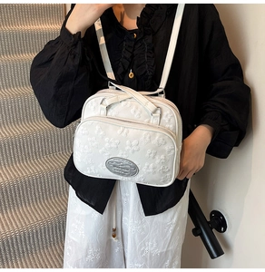 Détail du sac à bandoulière blanc avec broderie florale 3D et plaque logo argentée