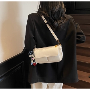 Close-up of cream pillow bag with leather texture and colorful charm on shoulder strap