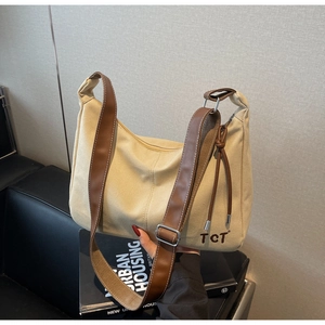 Detail der beigen Canvas-Tasche mit braunen Lederriemen und TCT-Logo auf schwarzem Sofa
