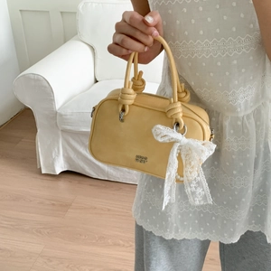 Detail der hellgelben Lederhandtasche mit dekorativer Schleife, Perlen und Knotengriff