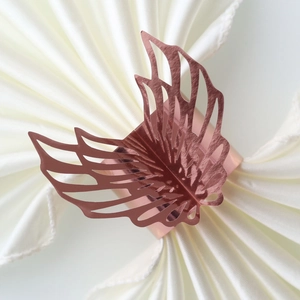 Macro shot of rose gold wing-shaped napkin ring with hollow design on white silk