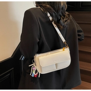 Detail of a creamy white glossy leather shoulder bag with gold hardware and pearl charm