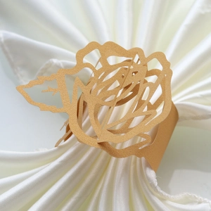 Detail of laser-cut rose paper napkin ring in matte gold on a white satin napkin