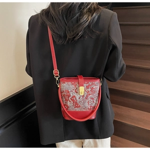 Detailed view of a red embroidered bucket bag with gold lock on a model's shoulder