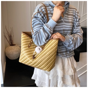 Detail of woven tote bag featuring yellow striped texture and brown leather shoulder straps