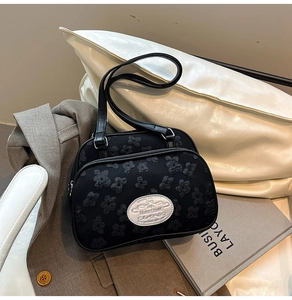 Détail d'un sac à main noir texturé à fleurs avec plaque en métal sur blazer gris